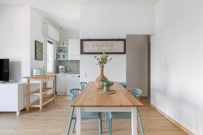 A modern kitchen with white cabinets, a microwave, and a toaster. There is a dining table with chairs and a vase with dried flowers. A framed picture of a coffee menu hangs on the wall. - Riva Apt · Lake View - Finestra sul Lago (Navene)