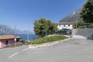 A coastal road with a stone wall, a parked car, and a building with a balcony overlooking the sea. - Riva Apt · Lake View - Finestra sul Lago (Navene)