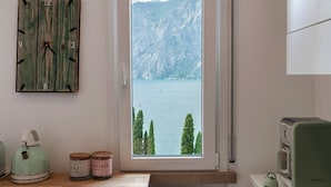 Ein Zimmer mit einer Holz-Wanduhr, einem Fenster mit Seeblick und Bergen, einem Vintage-Radio und einem Wasserkocher auf der Arbeitsplatte.
