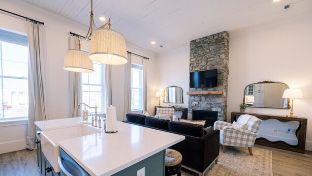 A modern kitchen with a central island, a stone fireplace, a flat-screen TV, and a cozy seating area with a sofa and armchairs.