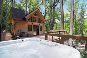 Una cabaña de madera con jacuzzi, terraza y un bosque de fondo.