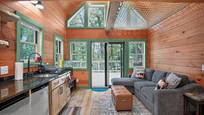 A cabin interior with a kitchen, dining area, and a living room with a sofa and ottoman.