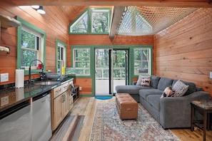 A cabin interior with a kitchen, dining area, and a living room with a sofa and ottoman. - The Beary Cozy Treehouse (Hendersonville)