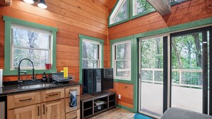 A wooden cabin interior with a kitchen area, a television, and large windows.