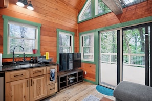 Interior de una cabaña de madera con cocina, televisor y ventanas amplias.