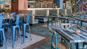 Interior de restaurante com vigas de madeira, cadeiras azuis e luminárias pendentes.