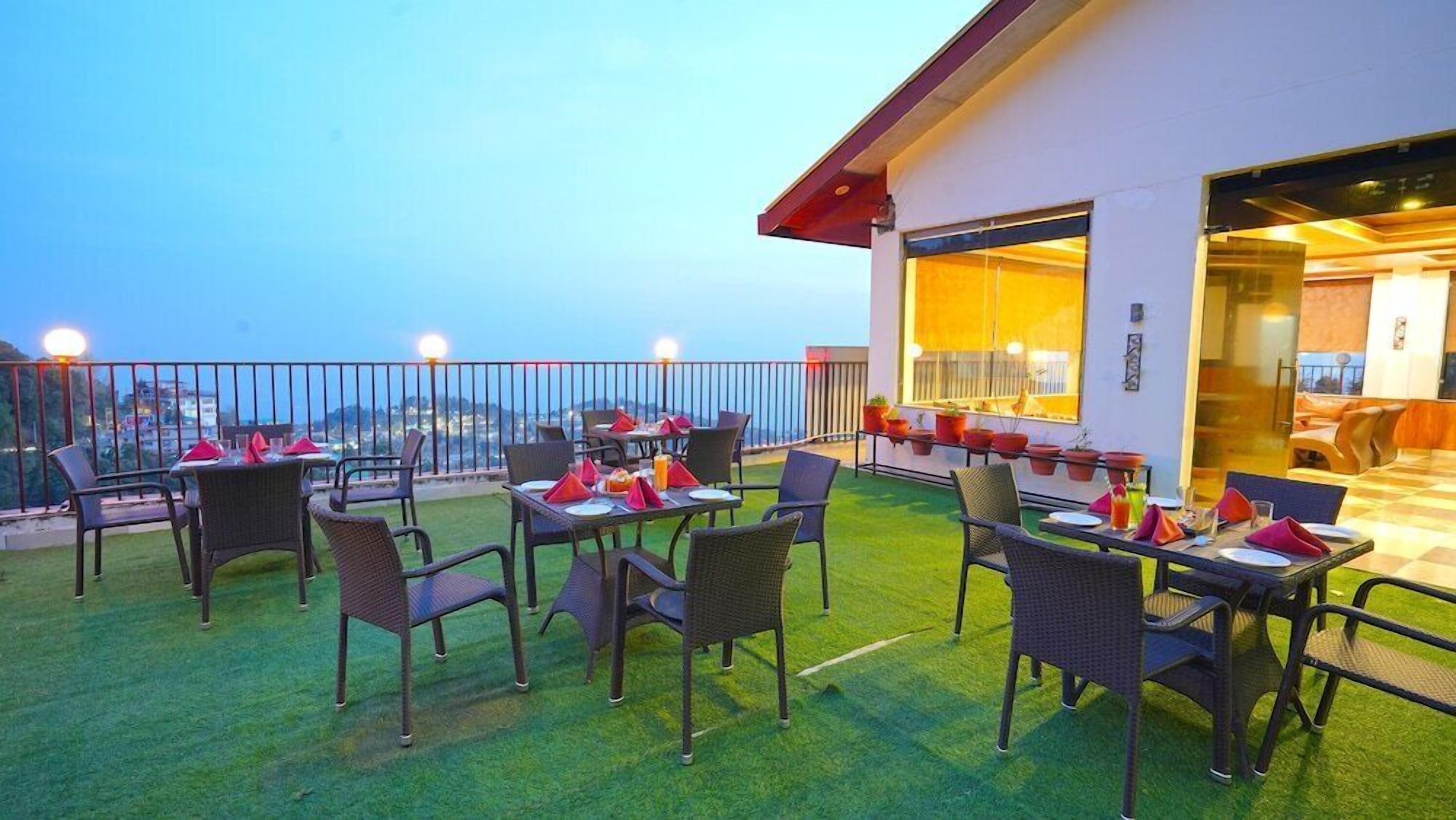 An outdoor dining area with tables and chairs, a view of the city, and a building entrance.