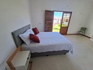 A bedroom with a bed, pillows, a nightstand, a door leading to a balcony, and a chair.