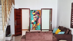 Een woonkamer met een bank, een televisie, een schilderij en een trap.