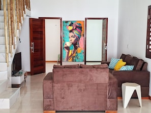 A living room with a sofa, a TV, a painting, and a staircase.