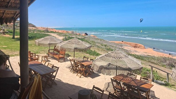 Een restaurant aan het strand met terras, rieten parasols en uitzicht op de oceaan.