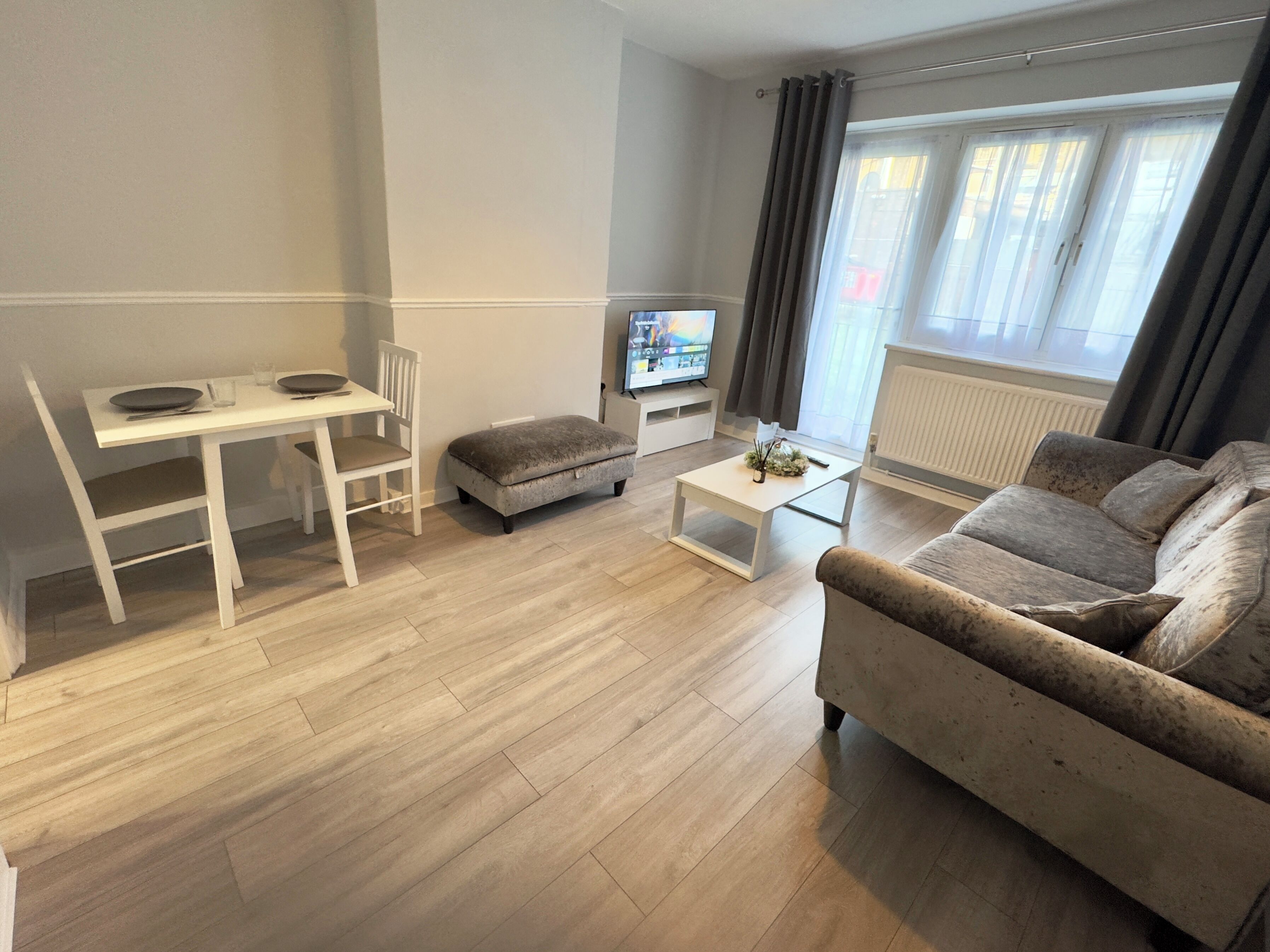 A modern living room with a white dining table, a grey sofa, a small ottoman, and a coffee table.