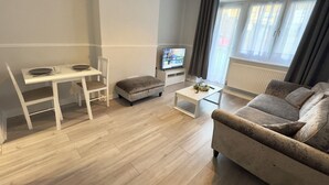 A modern living room with a white dining table, a grey sofa, a small ottoman, and a coffee table. - Modern 2 bedroom apartament in the heart of Greenwich (London)