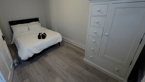 A bedroom with a bed, a white wardrobe, and a wooden floor. - Modern 2 bedroom apartament in the heart of Greenwich (London)