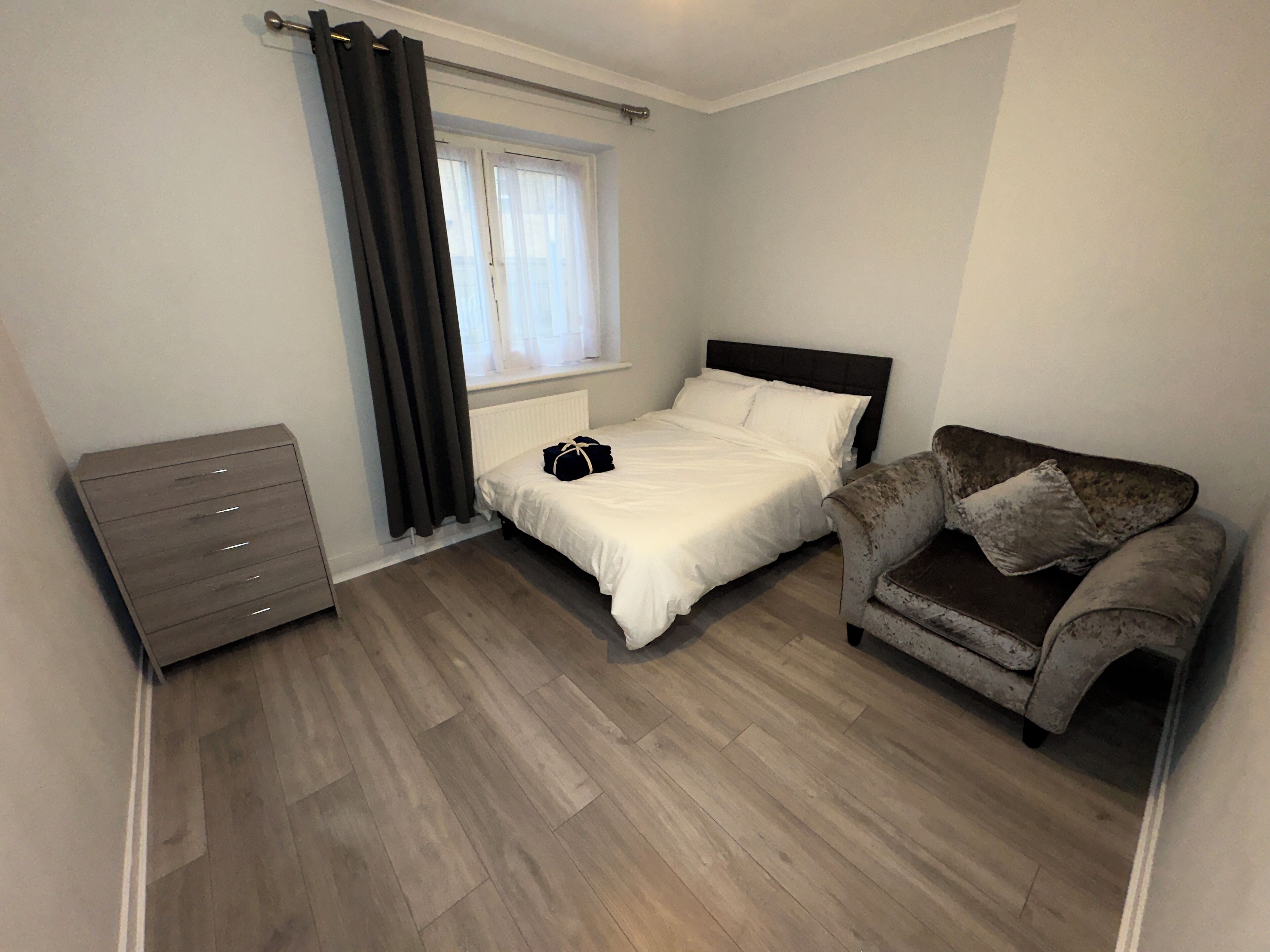 Une chambre à coucher avec un lit, une commode, une chaise et une fenêtre avec des rideaux.