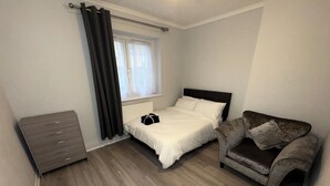 A bedroom with a bed, a dresser, a chair, and a window with curtains. - Modern 2 bedroom apartament in the heart of Greenwich (London)