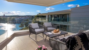 A modern balcony with wicker furniture, a glass table, and a view of a body of water and distant buildings. - Villa Krk - Luxury apartment by the sea with view of Krk town and shared pool (Krk (Krk))