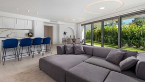 A modern living room with a grey sectional sofa, a dining area with blue chairs, and a kitchen with white cabinets. - Villa Krk - Luxury apartment by the sea with view of Krk town and shared pool (Krk (Krk))