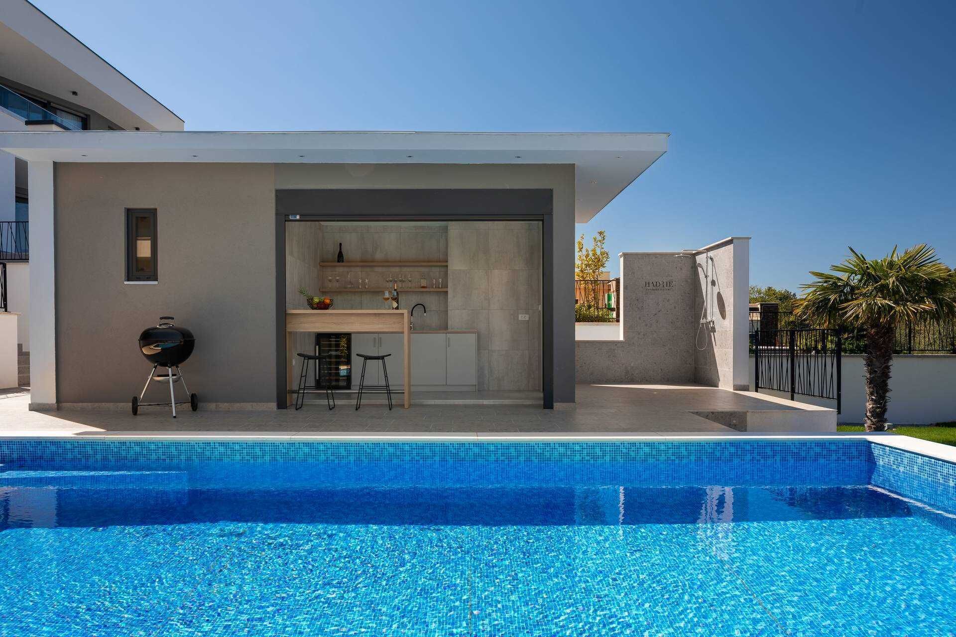Una cocina moderna al aire libre con una piscina al frente.