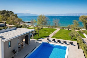 Un espace piscine extérieur moderne offrant une vue dégagée sur la mer et les montagnes en arrière-plan.