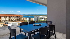 Een balkon met een tafel en stoelen, uitkijkend op een kustgezicht met gebouwen en een heldere lucht.