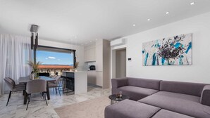 Een moderne woonkamer met een grijze modulaire bank, een eethoek met tafel en stoelen, en een keuken op de achtergrond.