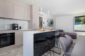 A modern kitchen with a central island, bar stools, and a seating area with a sofa. - Villa Rova – Luxury  Apartment with private pool and sea view (Malinska (Krk))