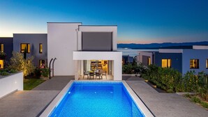 Ein moderner Poolbereich mit freiem Blick auf das Meer und die dahinterliegenden Berge.