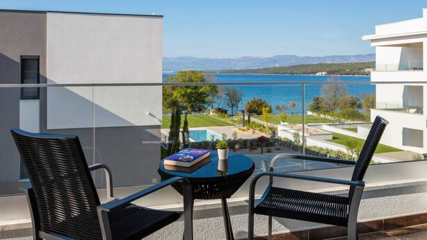 Ein Balkon mit zwei Stühlen und einem kleinen Tisch, mit Blick auf einen See und Berge.
