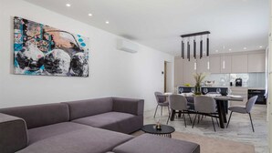 Ein modernes Wohnzimmer mit einem grauen Ecksofa, einem Essbereich mit Tisch und Stühlen und einer Küche im Hintergrund.