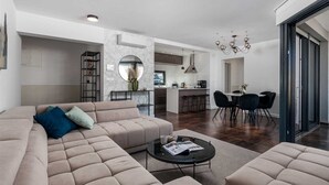 A modern living room with a sectional sofa, a coffee table, and a dining area with a chandelier. - Villa Rova – Apartment with a Seaview (Malinska (Krk))