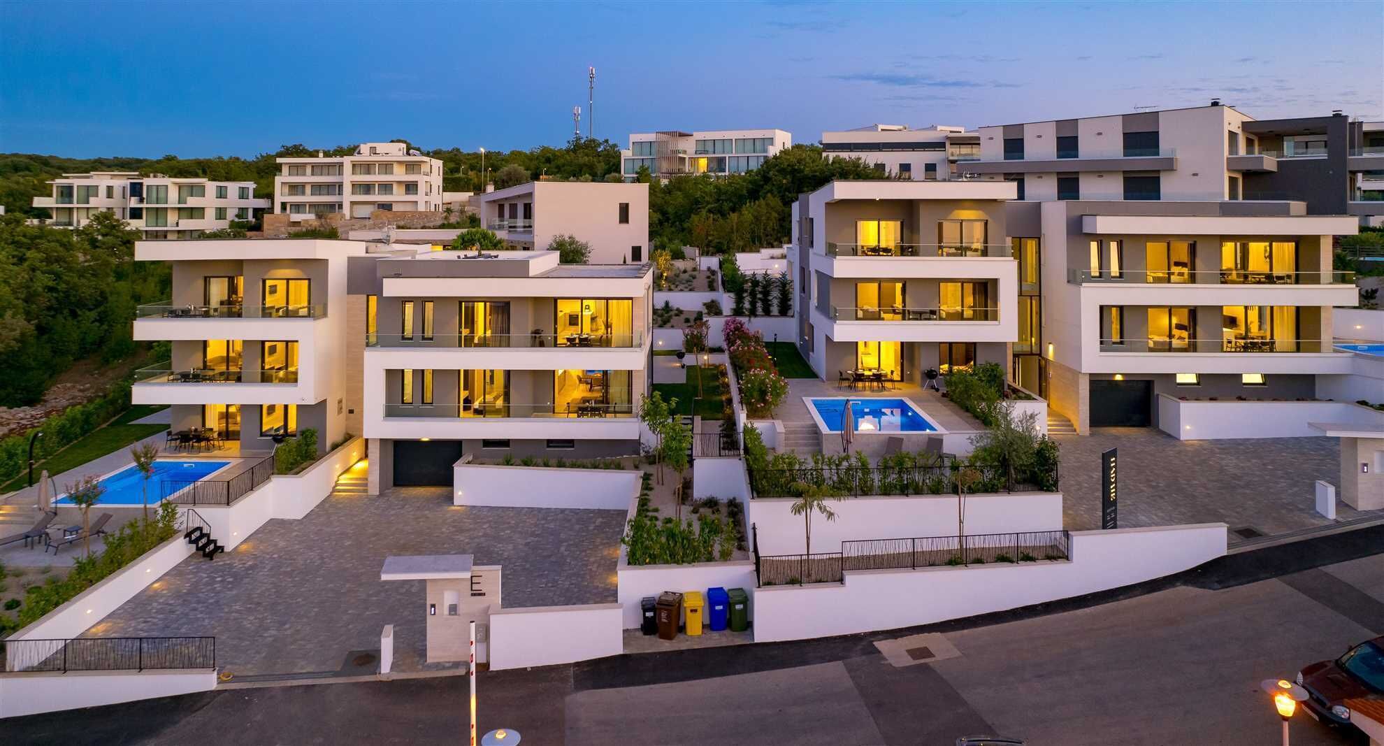 Ein moderner Wohnkomplex mit mehreren zweistöckigen Gebäuden, jedes mit Balkonen und einem Swimmingpool.