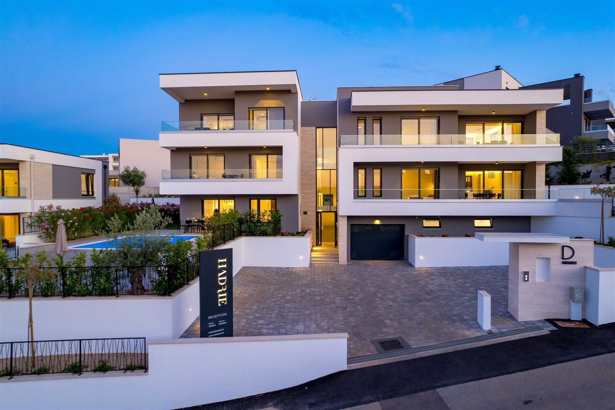 A modern multi-story residential building with a reception area, a swimming pool, and a well-maintained garden.
