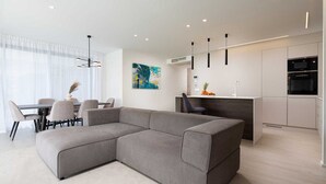 A modern living room with a grey sectional sofa, a dining area with a table and chairs, a kitchen with a microwave and a sink, and a painting on the wall. - Villas Azimut - Luxury Apartment with a Private Pool Near the Sea (Malinska (Krk))