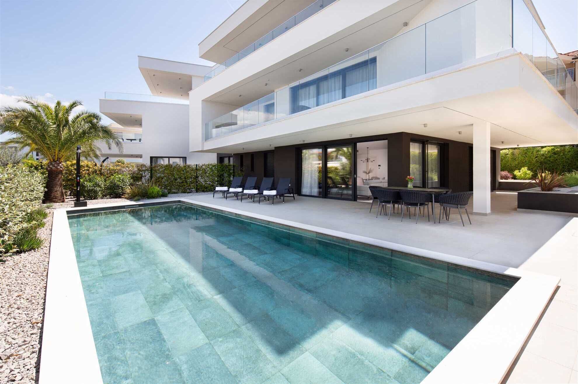 Ett modernt hus i två våningar med en swimmingpool, en uteplats och en välskött trädgård.