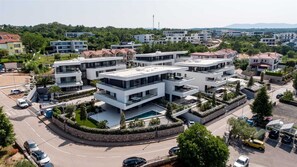 Ein moderner Wohnkomplex mit mehreren zweistöckigen Gebäuden, einem zentralen Innenhof mit Swimmingpool und einer umlaufenden, bepflanzten Grünfläche.