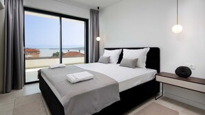 Ett modernt hotellrum med en stor säng, ett nattduksbord, utsikt över havet och ett stort fönster.