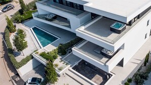 Ett modernt hus i flera våningar med en swimmingpool, utomhusmöbler och en bubbelpool.