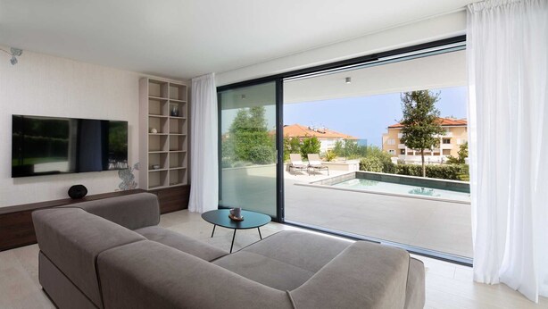 Un soggiorno moderno con un divano, una TV, un tavolino e un'ampia porta scorrevole in vetro che dà su una zona con piscina all'aperto.
