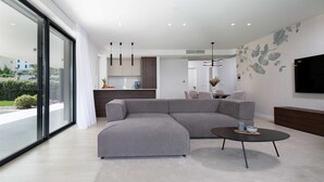 A modern living room with a grey sectional sofa, a round coffee table, and a flat-screen TV mounted on the wall. - Villas Azimut – Superior Apartment with Pool, Terrace and Stunning Sea View (Malinska (Krk))