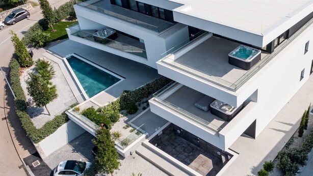 Ein modernes, mehrgeschossiges Haus mit Swimmingpool, Sitzgelegenheiten im Freien und Whirlpool.
