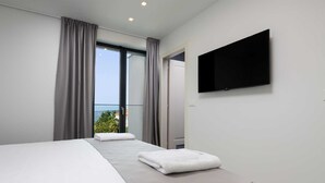 Ein modernes Hotelzimmer mit einem großen Bett, einem an der Wand montierten Fernseher und einem Balkon mit Meerblick.