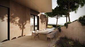 A modern outdoor dining area with a long table and chairs, surrounded by a low wall and greenery, overlooking a body of water.