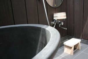 Una bañera con un taburete de madera al lado, un estante de madera pequeño y un espejo fijado a la pared.