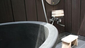 Un área de spa con una bañera negra grande, un taburete de madera y un espejo instalado en la pared.