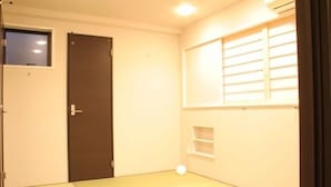 Una habitación pequeña y bien iluminada, con una puerta, una ventana con persianas y un estante pequeño.