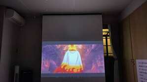 A projection screen in a room with a ceiling vent, a standing heater, and a wooden floor. - Casa Estacion Hikone (Hikone)