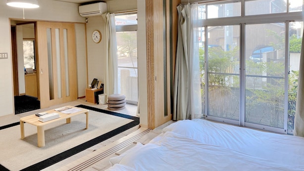 A hotel room with a bed, a small table, a clock, and a window with curtains. - Casa Estacion Hikone (Hikone)