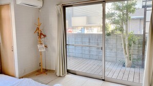 A hotel room with a bed, an air conditioning unit, a wooden drying rack, and a sliding glass door leading to a balcony with a view of buildings and trees. - Casa Estacion Hikone (Hikone)