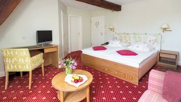 Une chambre à coucher comprenant un lit, un bureau, une chaise, une petite table avec des fruits et des fleurs, et un téléviseur.